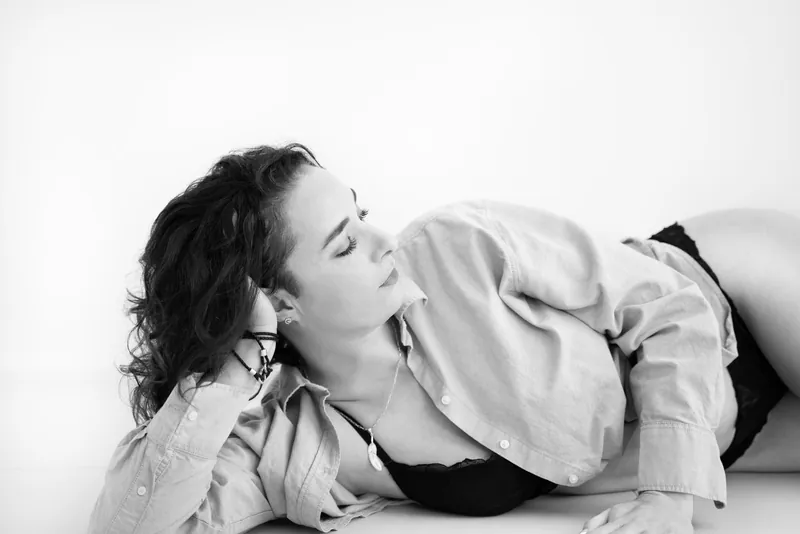 Black and white boudoir photograph of a woman lying in an open shirt
