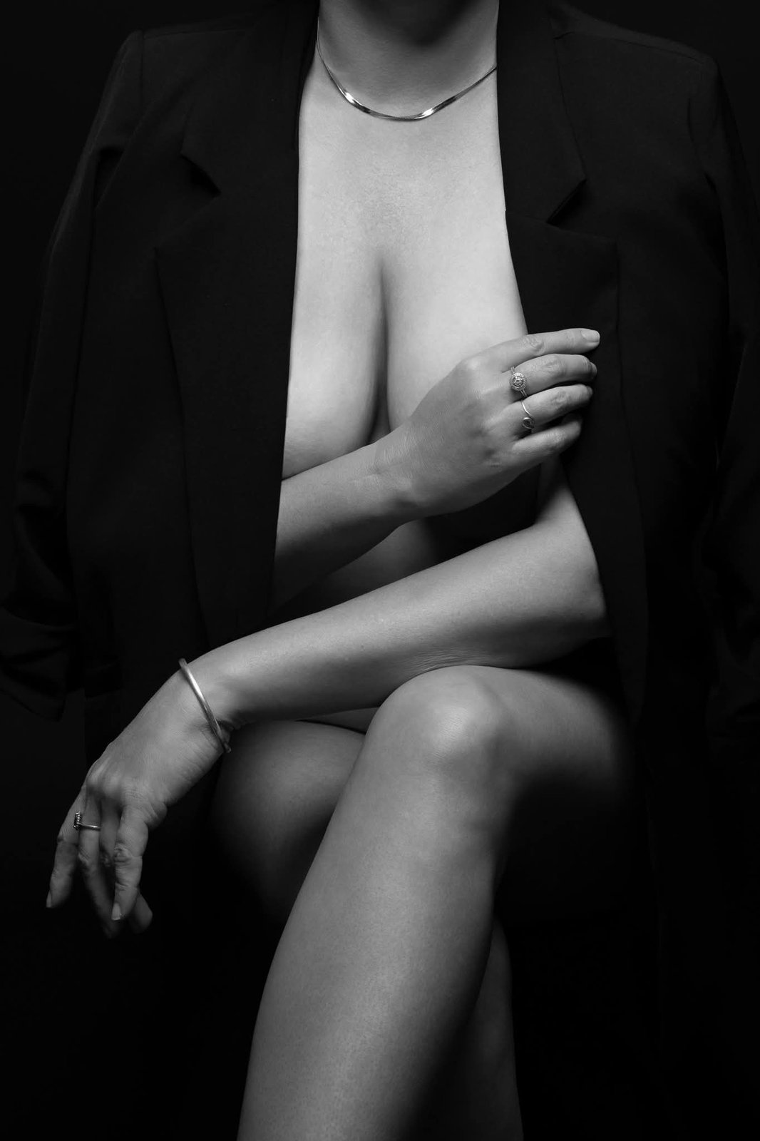 Black and white boudoir portrait of a woman seated in a black blazer