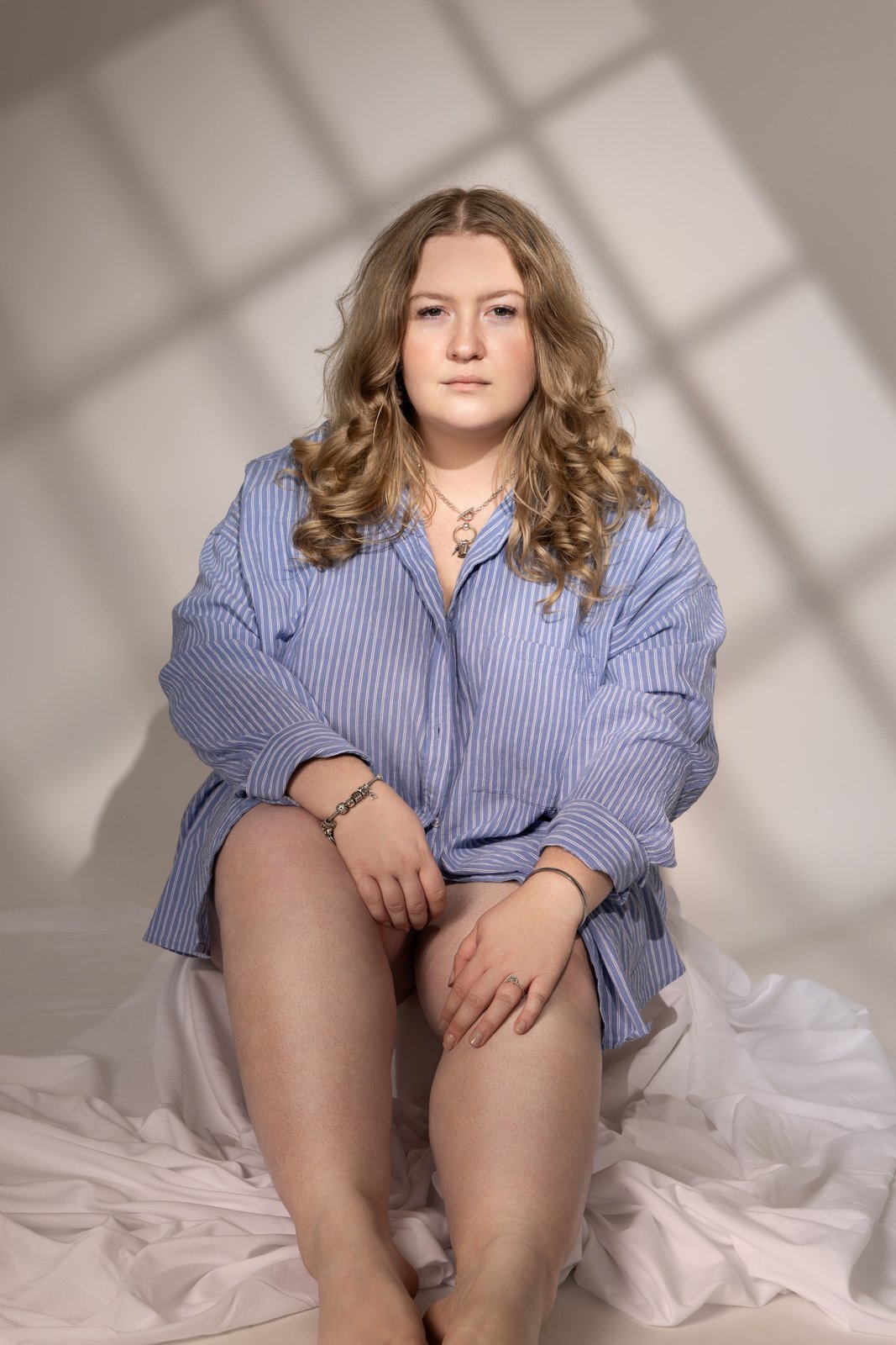 Boudoir portrait in an oversized blue shirt in window light